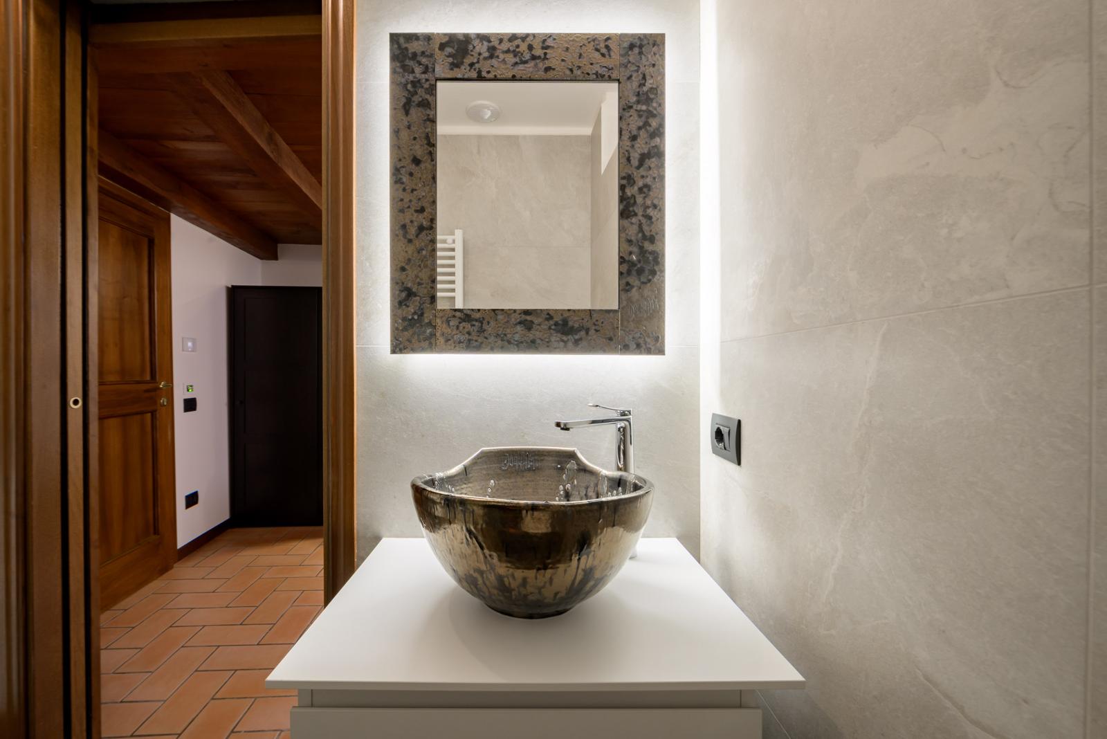 Bagno con lavabo artigianale in ceramica e specchio retroilluminato